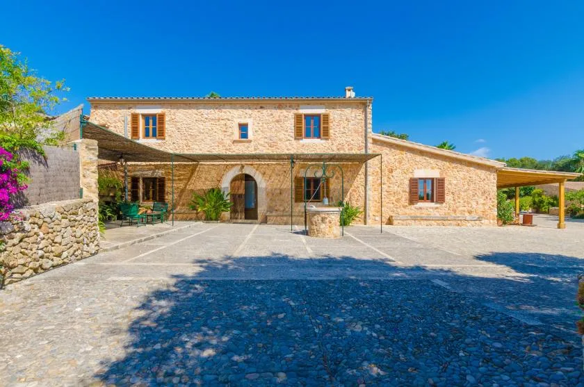 A stone house faces a paved courtyard under a clear blue sky.
