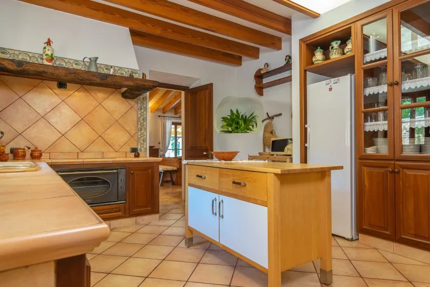 A warm-toned kitchen with wooden cabinets, tiled counters, and a central island.