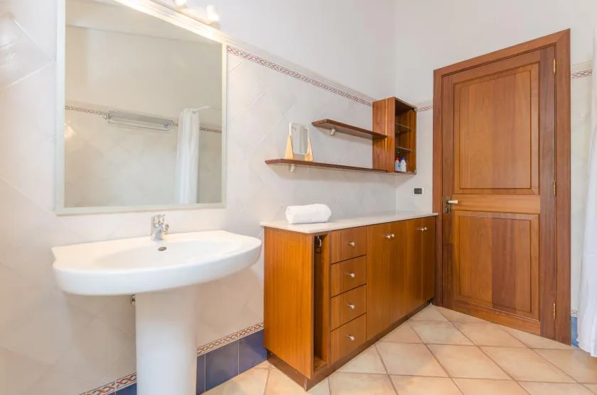 A tiled bathroom with a pedestal sink, mirror, wooden vanity, and door.