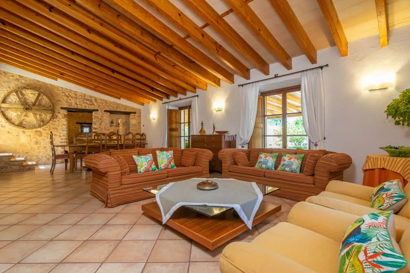 A living room with patterned seating, a coffee table, and exposed wooden ceiling beams.