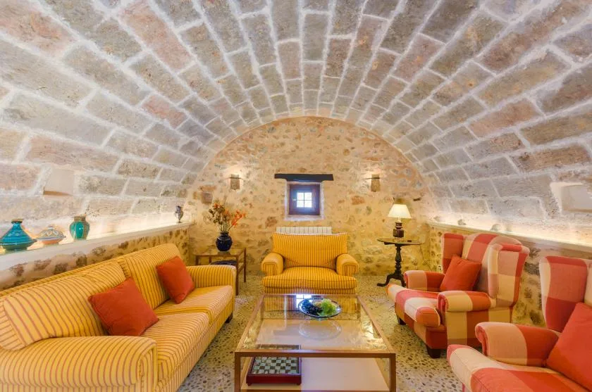 A furnished sitting room beneath a curved brick ceiling, with striped seating and a central table.