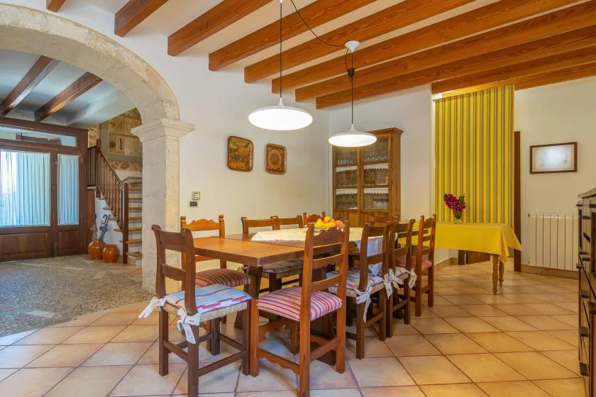 A dining room with a long wooden table and chairs beneath exposed ceiling beams.