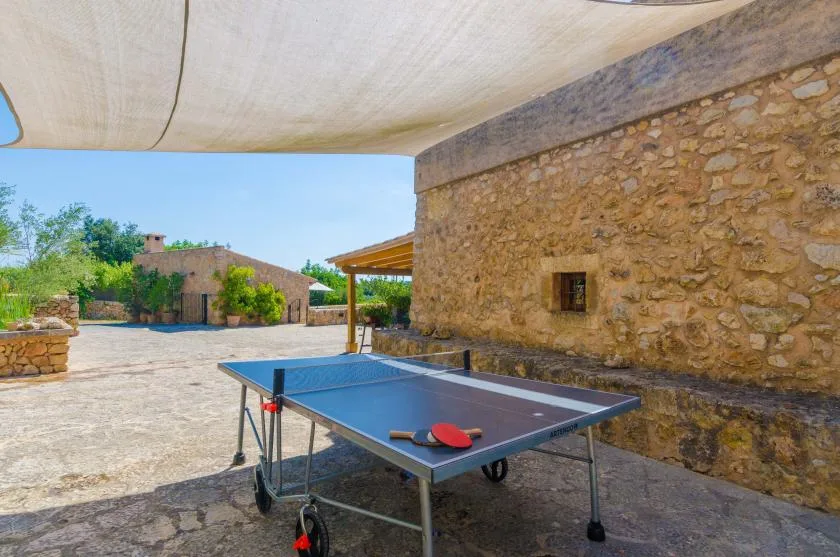 An outdoor patio features a ping-pong table beneath a shade canopy.