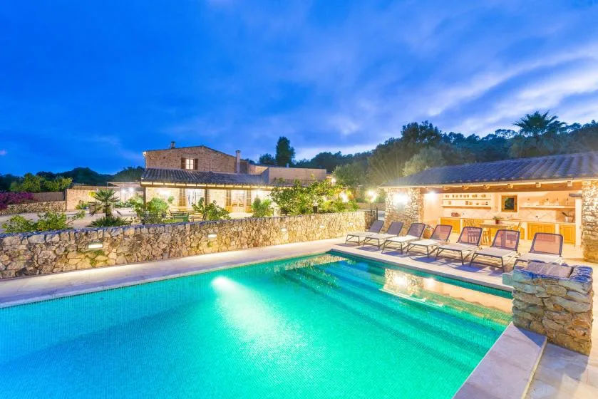 An outdoor swimming pool beside a stone terrace, illuminated in the evening.