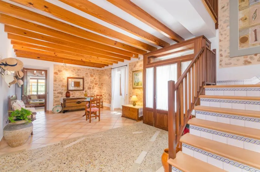 A rustic living area with exposed wooden ceiling beams and a staircase.