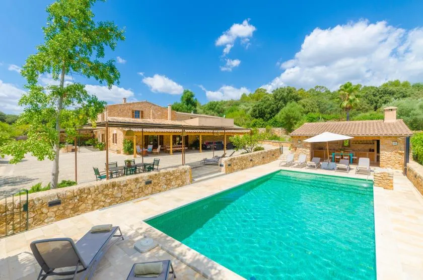 An outdoor swimming pool beside a stone patio and low buildings.