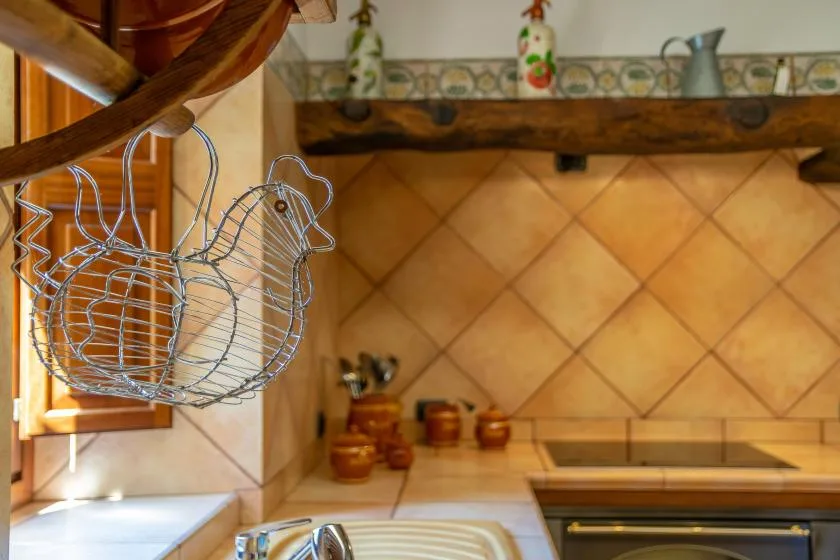 A tiled kitchen counter with a cooktop and wire kitchen rack hanging nearby.