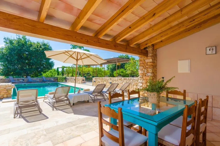 A covered outdoor dining area overlooks a swimming pool and patio seating.