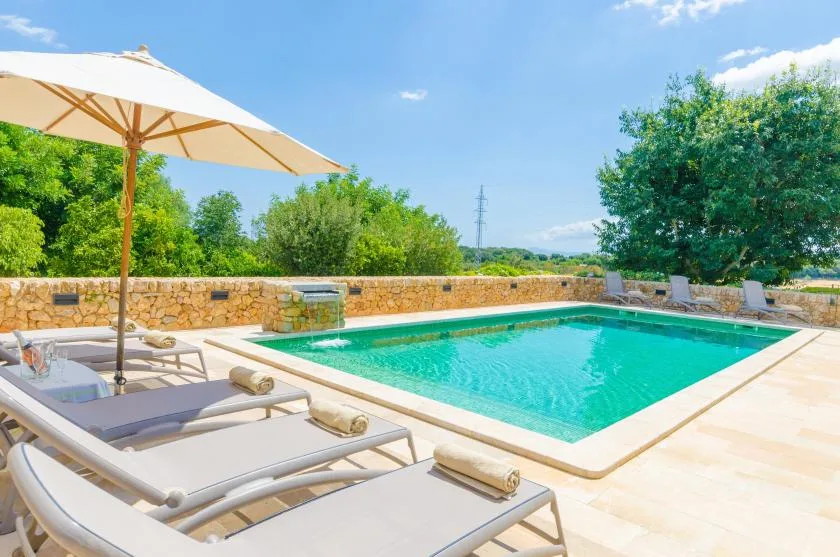 An outdoor swimming pool sits beside lounge seating and a large sun umbrella.