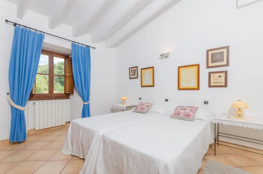 A bright bedroom with two beds, blue curtains, and framed pictures on the wall.
