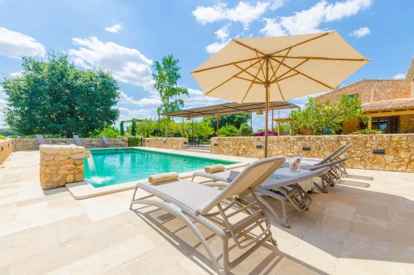A swimming pool beside a paved patio with lounge seating and a large umbrella.