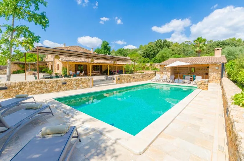 An outdoor swimming pool beside a stone terrace and shaded seating area.