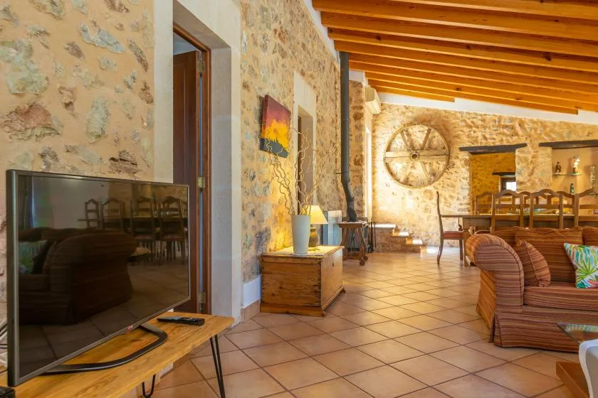 A stone-walled living room with a television, seating, and exposed wooden ceiling beams.