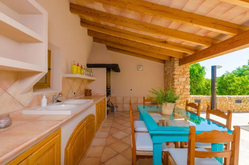 A covered patio dining area with a turquoise table beside a tiled counter.
