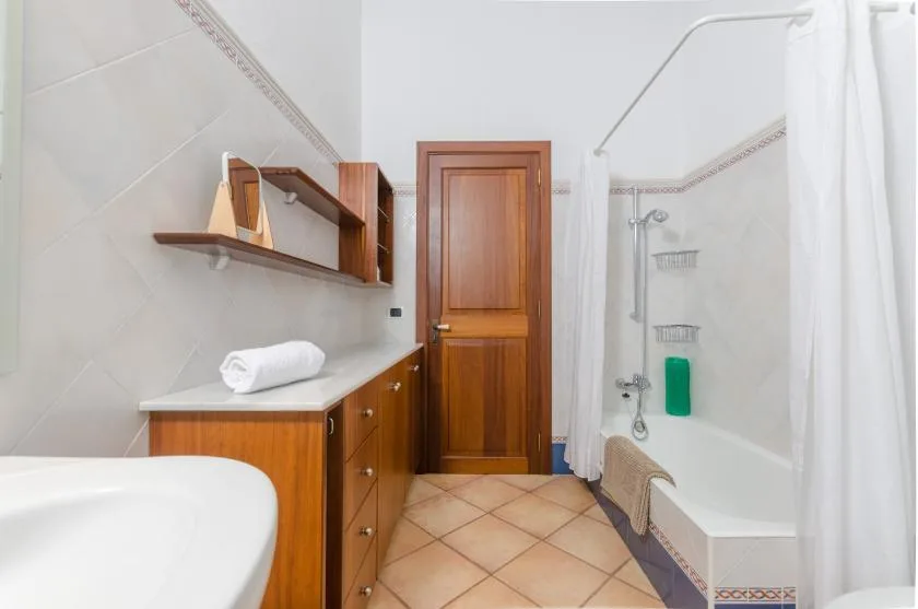 A tiled bathroom with a wooden vanity, sink, and bathtub with a shower curtain.