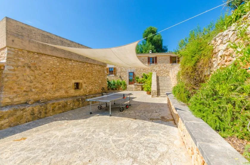 A stone courtyard with a table tennis table beneath a shade canopy.