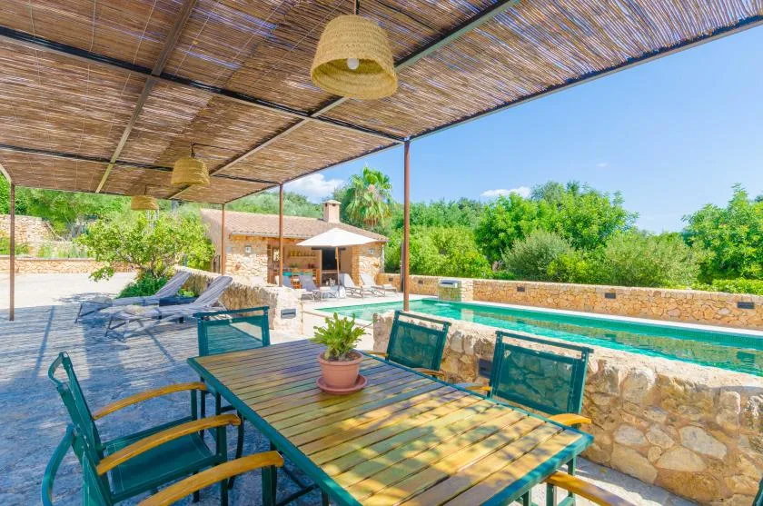 A shaded outdoor dining area overlooks a swimming pool and greenery.