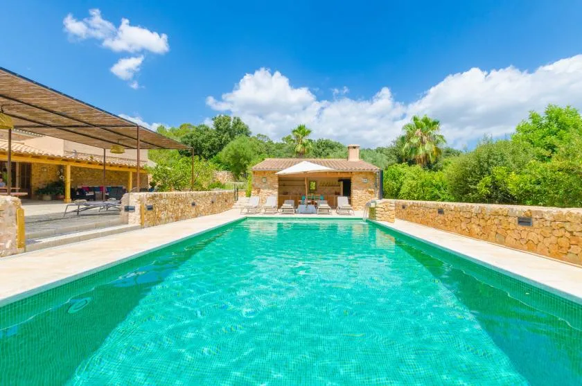 A swimming pool stretches toward a small poolside building and shaded seating area.
