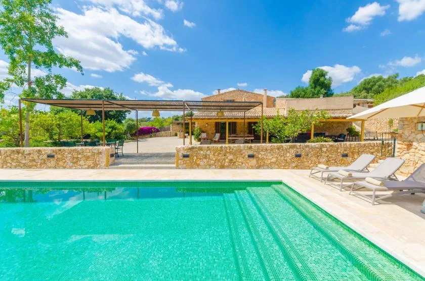 An outdoor swimming pool overlooks a stone terrace and a covered seating area.