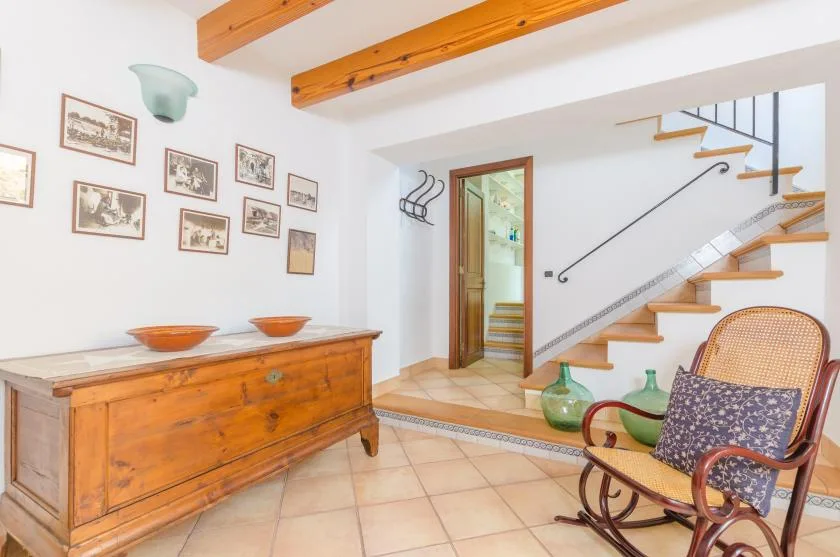 A bright tiled hallway with a wooden chest, framed pictures, and a staircase.