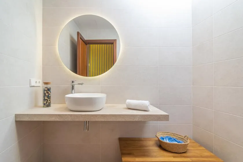 A tiled bathroom vanity with a round mirror, sink, and folded towel.