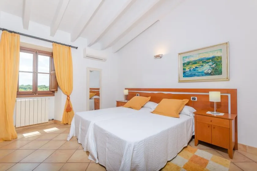 A bedroom with a double bed, orange curtains, and a framed painting.