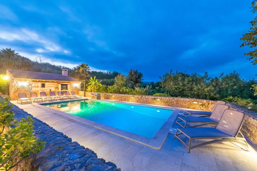 Outdoor swimming pool beside a lit building and lounge seating at dusk.