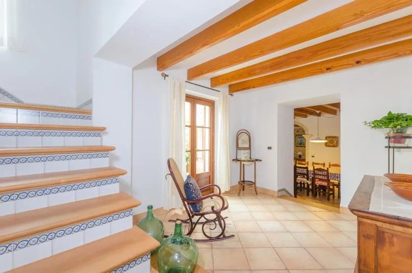 A tiled staircase and seating area open onto a dining room beneath exposed wooden beams.