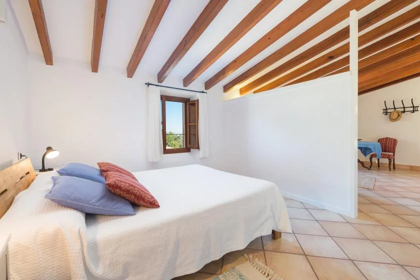 A bedroom with a white bed beneath exposed wooden ceiling beams.
