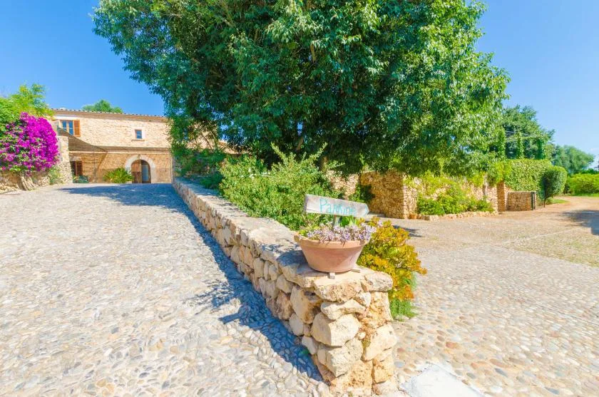 A cobblestone courtyard with a low stone wall, trees, and a stone building.
