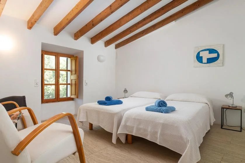 A bright bedroom with two beds and exposed wooden ceiling beams.