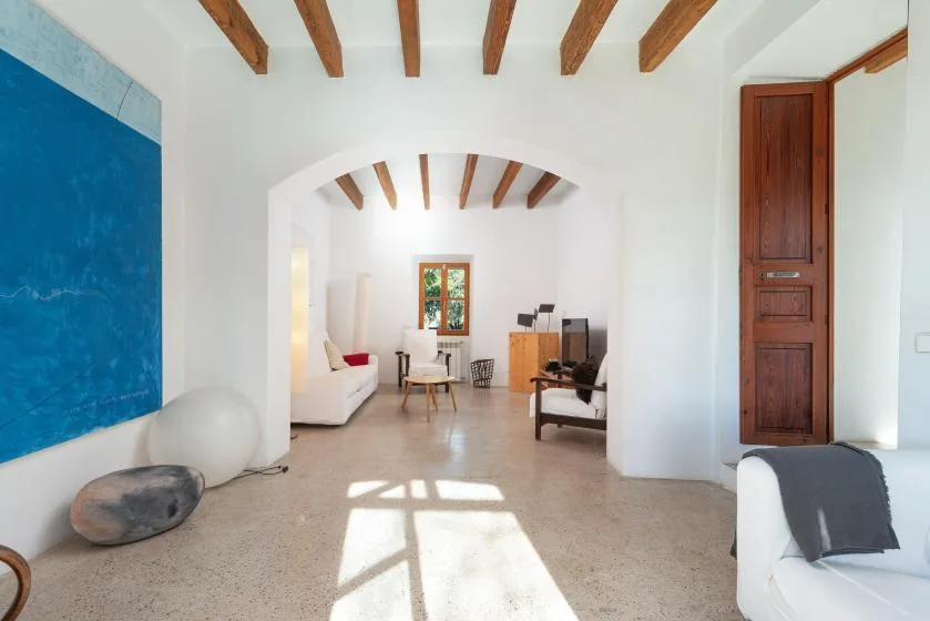 A bright living room with exposed ceiling beams and seating around a central archway.