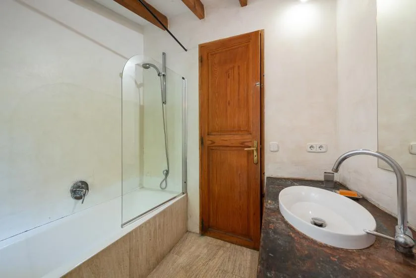 A bathroom with a shower, wooden door, and sink.