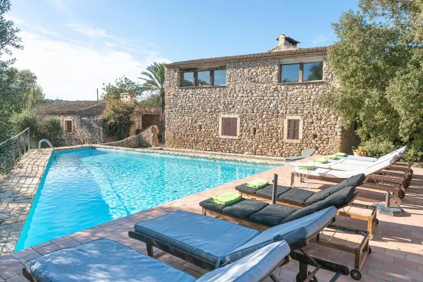 An outdoor swimming pool beside a stone building and lounge seating.
