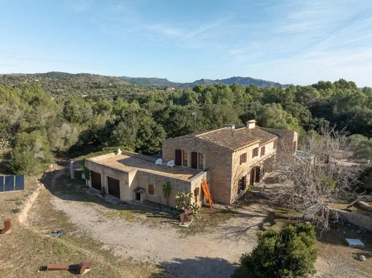 A stone house stands in a wooded landscape beneath a clear sky.