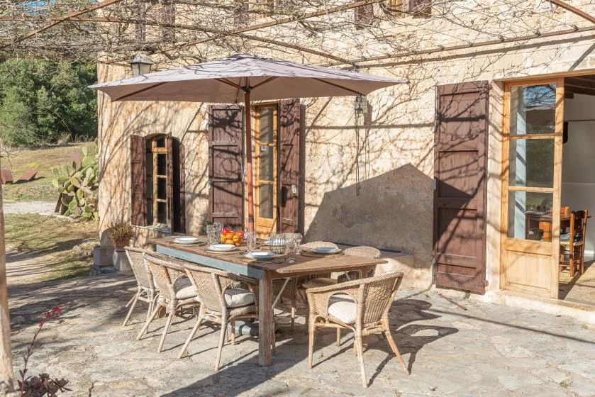 An outdoor dining area sits beside a stone building under a large umbrella.