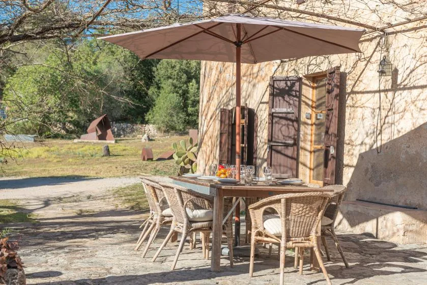 An outdoor dining area sits beneath a large umbrella beside a stone building.