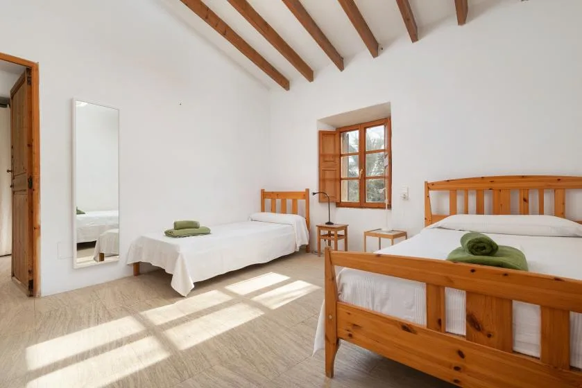 A bedroom with two wooden beds, a window, and exposed ceiling beams.