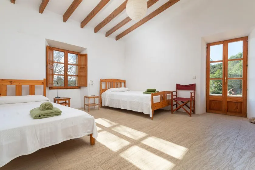 A bright bedroom with two beds and wooden ceiling beams.