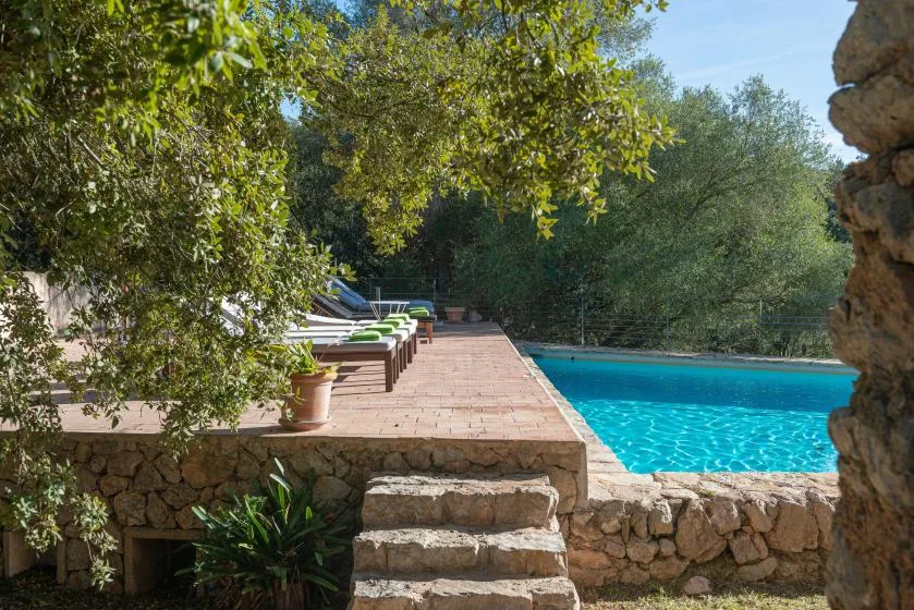 An outdoor swimming pool beside a stone terrace with lounge seating.