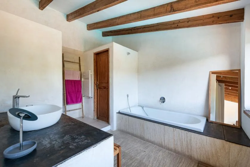 A bathroom with a bathtub, vessel sink, and exposed wooden ceiling beams.