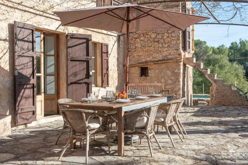 A stone courtyard with an outdoor dining table and chairs beneath a large umbrella.