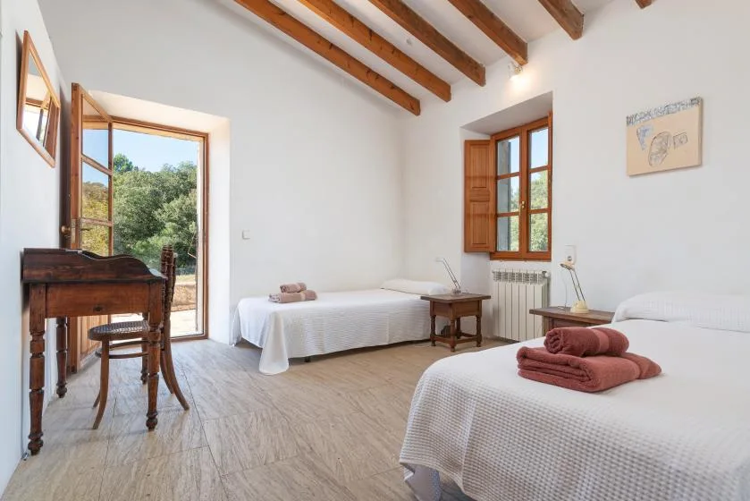 A bright bedroom with two beds and wooden ceiling beams.