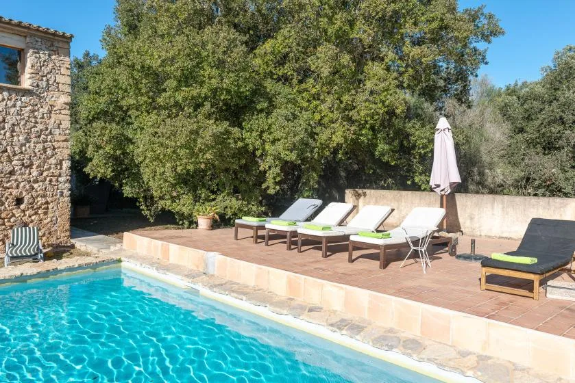 An outdoor swimming pool sits beside a tiled patio with lounge seating and an umbrella.