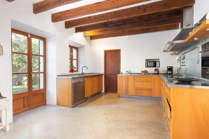 A bright kitchen with wooden cabinets, a countertop, and exposed ceiling beams.