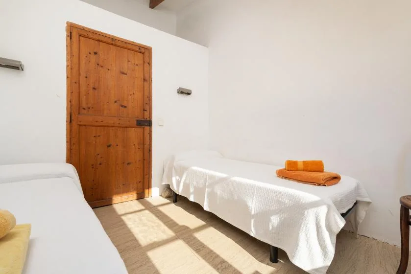 A bright bedroom with two beds covered in white linens and a wooden door.