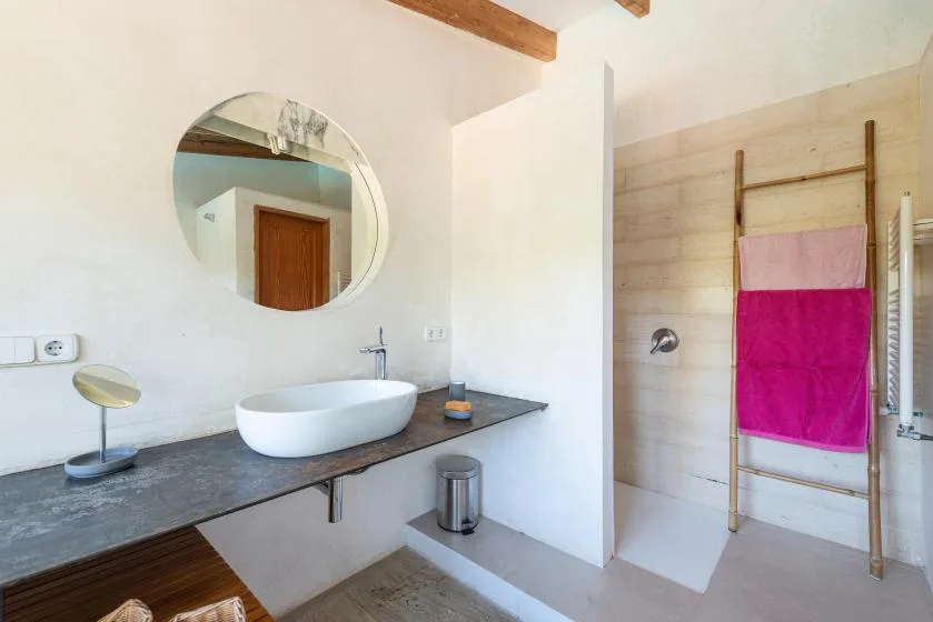 A bathroom vanity with a round mirror beside a shower area.