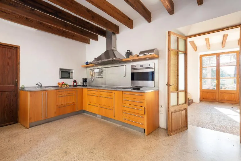 A kitchen with wooden cabinets, stainless steel appliances, and exposed ceiling beams.