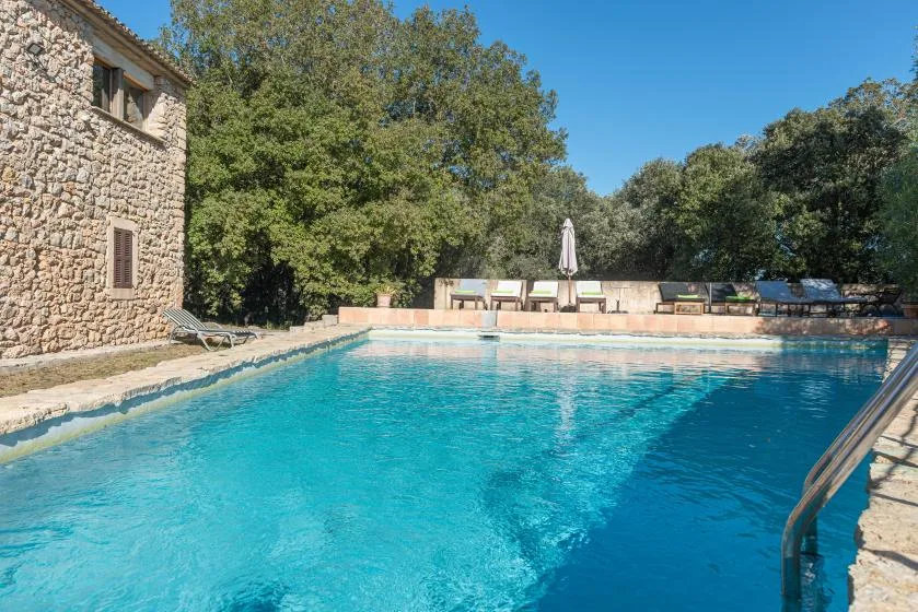 An outdoor swimming pool beside a stone building, with trees and seating in the background.