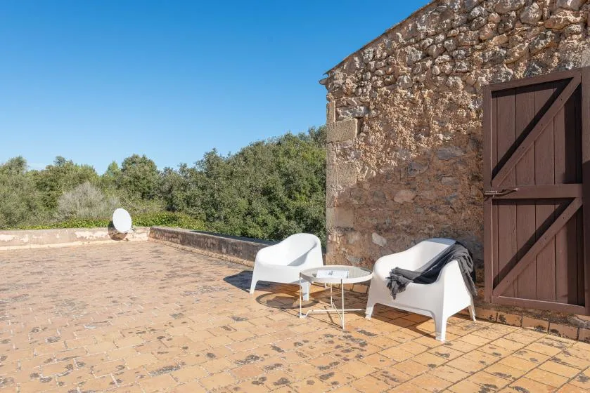 A sunlit stone terrace with two white seats beside a rustic wall.